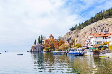Ohri Gölü 'nün güzel sonbahar manzarası. Kaneo' daki tarihi St. John Kilisesi kayalıklara tünemiş, etrafı tekneler ve deniz kenarındaki evlerle çevrili..