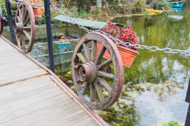 Kırsal tekerlek korkulukları çiçek saksılarıyla bezenmiş büyüleyici ahşap köprü, yemyeşil yemyeşil bir göletin üzerinden geçiyor..