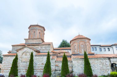 Muhteşem St. Naum Manastırı, Ohri Gölü boyunca, Bizans mimarisi, Doğu Ortodoks manastırı, geleneksel taş mimarisi ve kırmızı çatıları, kasvetli gökyüzü.