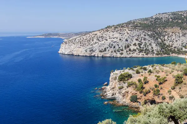 Dalgalı derin mavi denize düşen engebeli, kayalık uçurumların nefes kesici manzarası. Güneşli bir gökyüzünün altında dramatik kıyı manzarasını ve berrak suyu vurgular.