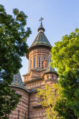 Timisoara Ortodoks Katedrali 'nin zarif kulelerinin ve zengin yeşil yapraklarla kısmen çerçevelenmiş titreşimli kubbelerinin huzurlu manzarası.