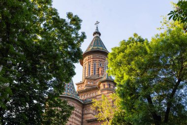 Timisoara Ortodoks Katedrali 'nin zarif kulelerinin ve zengin yeşil yapraklarla kısmen çerçevelenmiş titreşimli kubbelerinin huzurlu manzarası.