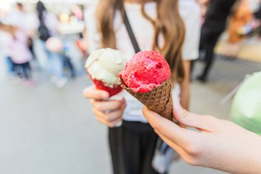 Kahverengi Waffle Konilerinde Kırmızı ve Beyaz Scoops 'lu iki dondurma külahı.