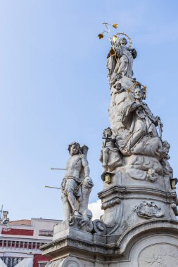 Romanya 'nın Timisoara kentindeki tarihi Özgürlük Meydanı' nda belirgin bir şekilde duran, birden fazla figür ve heykelle süslenmiş uzun ve süslü taş bir heykelin ayrıntılı manzarası.