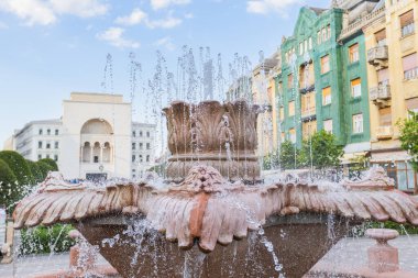 Timisoara 'nın canlı Zafer Meydanı' ndaki (Piata Victoriei) süslü Balık Çeşmesi 'nin yakın çekimleri, Romanya Ulusal Opera cephesi de dahil olmak üzere tarihi binaların bir zeminine püskürtülen suyu yakalıyor..