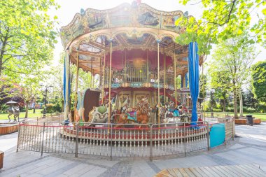 Vintage Double-Decker Carousel with Ornate Decorations and Painted Horses in Public Park Surrounded by Trees clipart