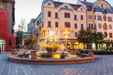 Gece boyunca Romanya 'nın Timisoara kentindeki Piata Victoriei (Zafer Meydanı) kentindeki canlı çeşmenin manzarası. Meydanın kendine özgü tarihi mimarisi ile çevrili..