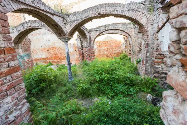 Büyük ölçüde yeşil bitki örtüsüyle kaplanmış birden fazla kemer ve duvarın bulunduğu tarihi bir binanın tuğla kalıntıları..