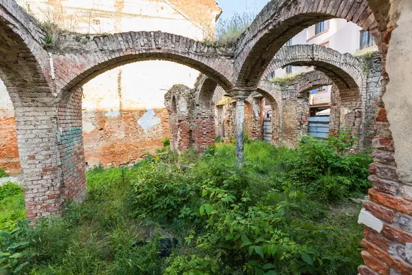 Büyük ölçüde yeşil bitki örtüsüyle kaplanmış birden fazla kemer ve duvarın bulunduğu tarihi bir binanın tuğla kalıntıları..