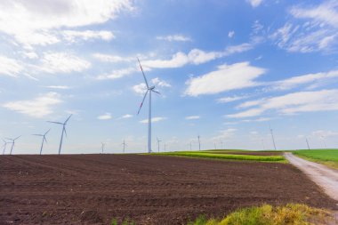 Parlak, bulutlu bir gökyüzü altında kırsal alanda temiz ve yenilenebilir enerji üreten çoklu modern rüzgar türbinlerinin manzarası..