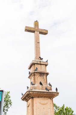 Tanınmış taş haç heykeli, Sırbistan 'ın Vrsac kentinde tüneyen güvercinlerle süslenmiş sakin bir halk parkında veya meydanda duruyor..