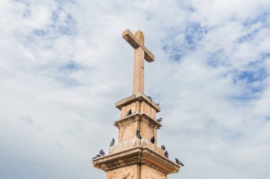 Tanınmış taş haç heykeli, Sırbistan 'ın Vrsac kentinde tüneyen güvercinlerle süslenmiş sakin bir halk parkında veya meydanda duruyor..