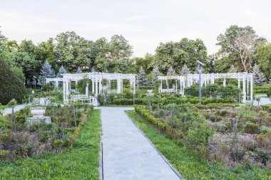 Beyaz Pergola Yapılarıyla Güzel Gül Parkı Bahçesi ve Taş Yataklarla bağlanmış Organize Çiçekler Romantik açık hava eğlencesi ve rahatlama için
