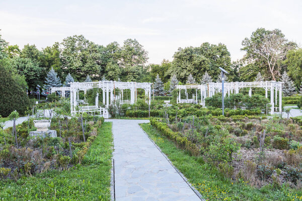 Сад "Розовый парк" с белыми перголовыми конструкциями и организованными клумбами у каменных дорожек для активного отдыха и релаксации на открытом воздухе
