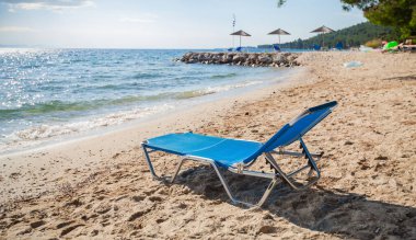 Kristal suları ve dağ manzaralı Sandy Yunan adasındaki mavi sahil sandalyesi Mükemmel rahatlama noktası