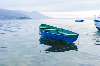 Alacakaranlıkta dingin bir gölün sakin sularında küçük mavi bir tekne dinlenir..