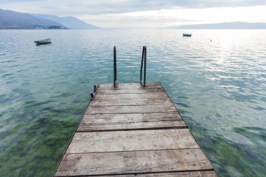 Bulutlu bir günde Tekneler ve Dağlık Ufuk ile Sakin Göl 'e Bakan Ahşap İskele