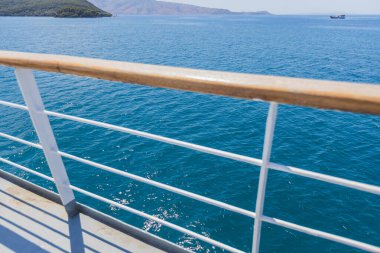 Bir teknenin güvertesinden huzurlu ve geniş açılı bir çekim. Derin mavi denizin engin genişliğini gösteriyor. Uzak dağlık bir kıyı şeridi.