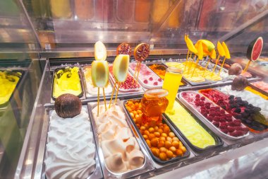 Dondurmanın çeşitli aromaları, taze meyve süslemeleri, çikolata süslemeleri ve profesyonel soğutmalı vitrinde renkli malzemeler içeren canlı dondurma sergisi..