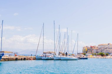 Berrak mavi bir gökyüzü altında canlı kıyı mimarisi tarafından çerçevelenmiş sakin bir limana demirlenmiş yelkenlilerin resimli görüntüsü. Sakin sular sakin atmosferi yansıtır. Seyahat, tatil ya da deniz teması için idealdir..