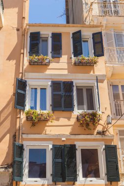 Eski Korfu Kasabası 'ndaki geleneksel Venedik tarzı bir binanın detaylı bir görüntüsü, berrak mavi gökyüzünün altında canlı panjurlar ve pencere çiçek kutuları yer alıyor..