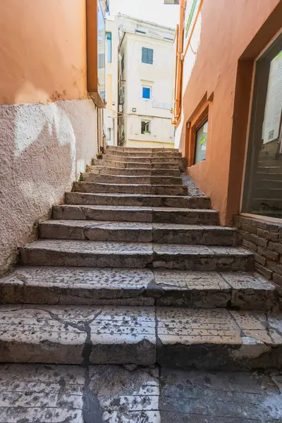 Tarihi Corfu kasabasının eski semtinde, renkli duvarları olan geleneksel Akdeniz binaları arasındaki dar geçitten yükselen yıpranmış taş merdivenler..