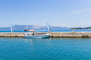 Küçük beyaz bir tekne Corfu 'da beton bir iskeleye demirlemiş, sakin mavi deniz uzak, puslu dağlara doğru uzanıyor..