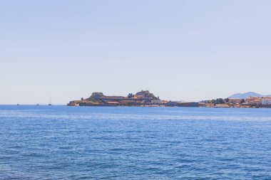 Kristal mavisi Akdeniz sularıyla çevrili tarihi kale adasının panoramik manzarasında antik taş tahkimatları ve geleneksel kıyı mimarisi, açık gökyüzü sergileniyor. Korfu, Yunanistan.