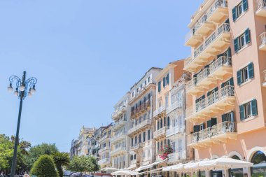 Geleneksel balkonları ve yeşil panjurları olan bir dizi tarihi, pastel renkli bina Yunanistan 'ın Korfu Kasabası' nda güneşli bir caddede sıralanır..