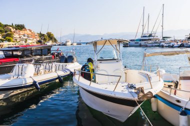 Beyaz balıkçı tekneleri ve lüks yatlar Yunan marinasında demirlemiş geleneksel terasotta çatılı köy evleri yamaçlara tırmanıyor..