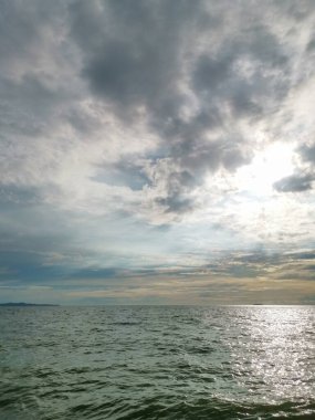 Gökyüzü bulutlu ve okyanus sakin. Güneş bulutların arasında parlıyor. Su açık mavi bir renktir.