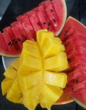 Bir dilim karpuz ve bir dilim mango ile tabak. Karpuz parçalara ayrılır ve mango da parçalara ayrılır.