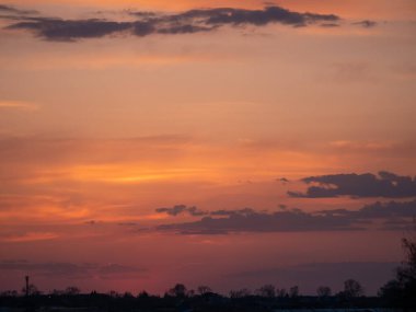 Güneş batarken gökyüzü güzel turuncu bir renktir. Bulutlar gökyüzüne dağılmış, huzurlu ve huzurlu bir atmosfer yaratıyorlar.