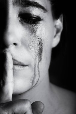 Makyajlı ve gözle görülür göz yaşları içinde bir kadın sessizce başını eğiyor, ellerini ağzına yaklaştırıyor.