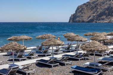 Kamari, Santorini, Yunanistan - 29 Haziran 2021: Santorini 'deki siyah volkanik Kamari plajında güneşlik. Cyclades, Yunanistan