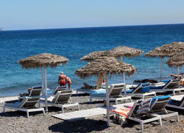 Kamari, Santorini, Yunanistan - 30 Haziran 2021: Santorini 'deki siyah volkanik Kamari plajında güneşlik. Cyclades, Yunanistan
