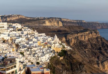 Yunanistan 'ın Kiklad adasındaki Santorini Adası' nda beyazlatılmış Fira kasabası gün batımının ılık ışınlarıyla