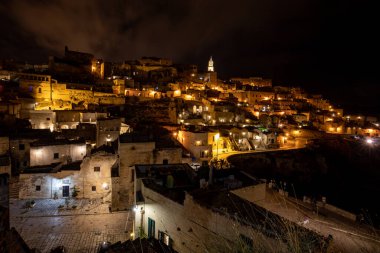 Matera 'daki antik Sassi bölgesinde geceleri, antik mağara evleri ile tanınan şaşırtıcı aydınlık binalar. Basilicata. İtalya