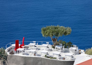 Oia, Santorini, Yunanistan - 3 Temmuz 2021: Oia, Santorini, Yunanistan 'da günbatımı manzaralı restoranların terasında masalar.