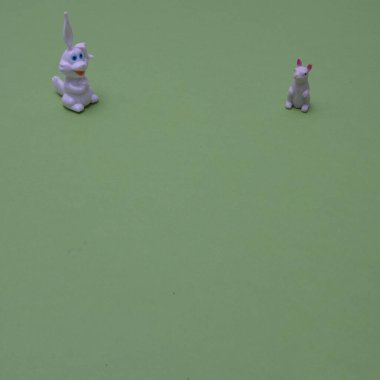Two white rabbits on a green surface with copy space, on the upper part of the background. Minimal scene for Chinese New year.
