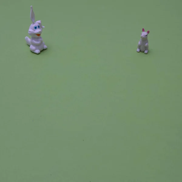 Two white rabbits on a green surface with copy space, on the upper part of the background. Minimal scene for Chinese New year.