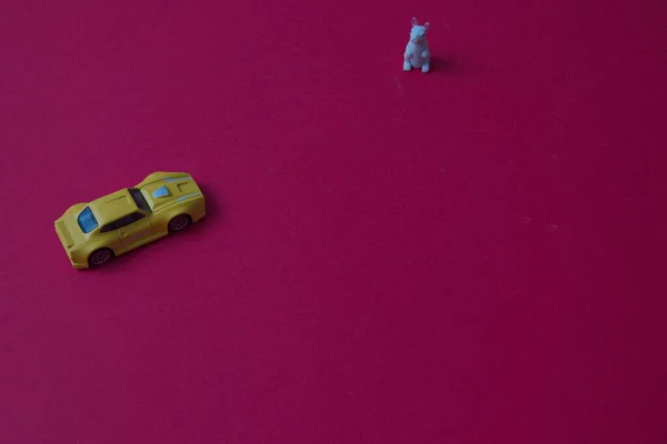 A white rabbit is waiting for a yellow car coming towards him on a red background with copy space. Minimal composition for Chinese New Year.