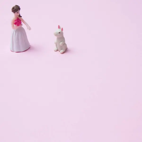 Bride with flowers in hand and wedding dress standing in front of white rabbit with outstretched hand on pink background with copy space. Minimalistic love scenes with Chinese New Year elements.