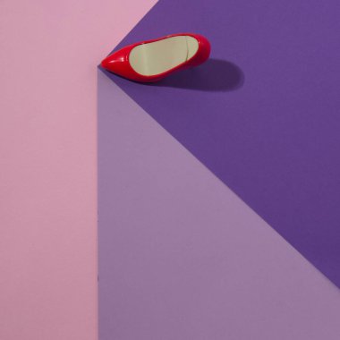 Red women's high heel on the edge of a purple cube on a pink background. Minimal flat lay composition.