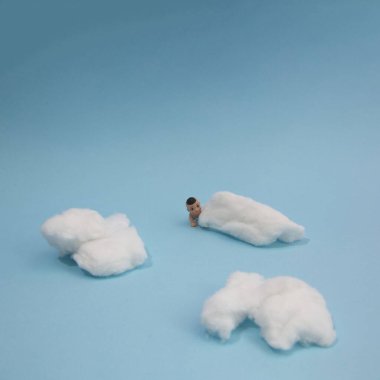 Bir bebek gökyüzündeki bulutların arasında sürünüyor, mavi arka planda kopya alanı var. Asgari sanatçı sahnesi.