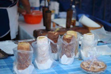 A group of colorful pastries wrapped in plastic sit atop a wooden table, beckoning with sweet aromas of freshly-baked bread and tempting taste of delectable desserts, inviting friends and family to gather and enjoy a warm snack indoors