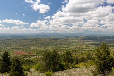 Uçsuz bucaksız bir manzara, yuvarlanan tepelerle çevrili geniş yeşil bir vadiyi, kabarık bulutlarla kaplı parlak bir gökyüzünün altında sergiliyor. Sahne huzurlu ve huzurlu, davetkar bir keşif..