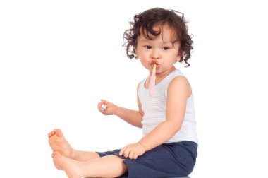 Kıvırcık saçlı bebek diş fırçasıyla dişlerini fırçalıyor ve beyaz arka planda diş macunu tutuyor.