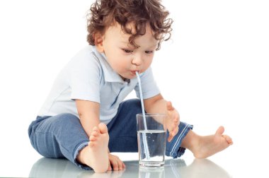 Şirin kıvırcık saçlı çocuk, bir bardakta su içiyor. Arkaplanda mutlu bir gülümseme var.