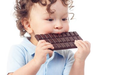 Kıvırcık saçlı, tatlı çikolata yiyen, beyaz arka planda mutlu bir gülümsemesi olan bir bebek.